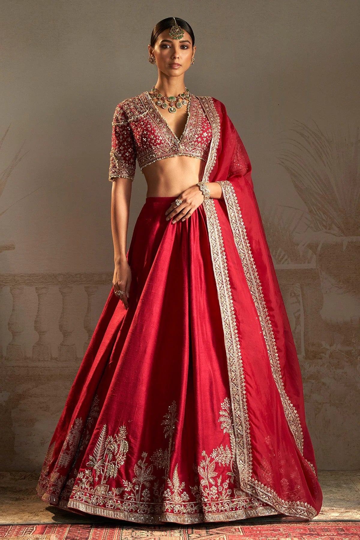 Full-length view of a crimson red lehenga with gold-tone floral embroidery, matching blouse and bordered dupatta